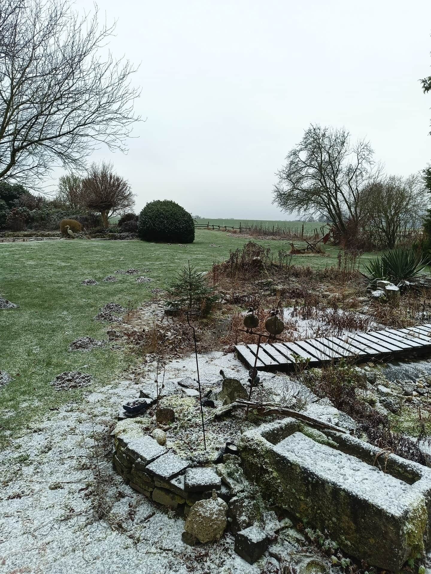 Un jardin agrémenté d’une structure en pierre, d’un pont en bois et d’un champ d’herbe.