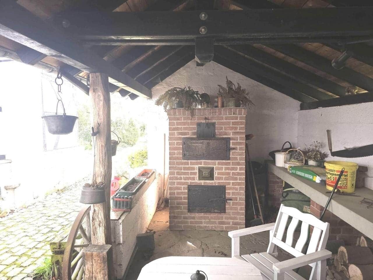 Un espace de cuisine extérieur rustique, doté d’un four en briques, de poutres en bois et de divers ustensiles de cuisine.