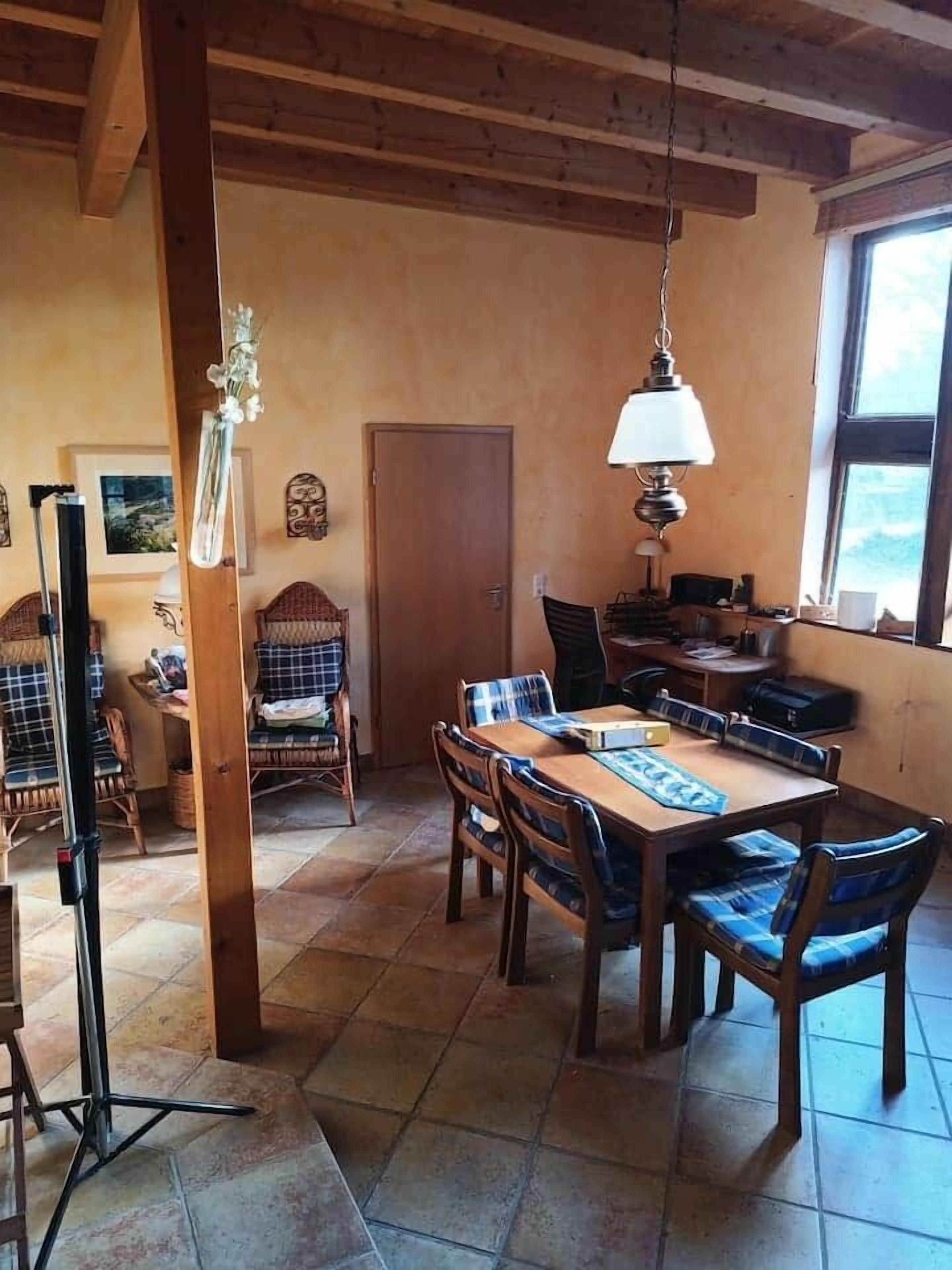 Un'area pranzo con tavolo e sedie in legno, una lampada a sospensione e vista all'esterno attraverso una finestra.