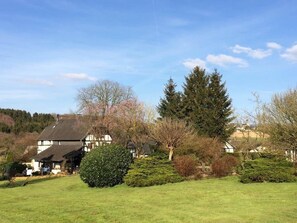 A residential area with a house featuring a large front lawn, a well-maintained garden, and a variety of trees including a prominent evergreen. - Kitchen-living room with bathroom in a historic barn (Hennef)