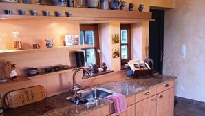 A kitchen with wooden cabinets, a granite countertop, and various kitchenware displayed on shelves. - Kitchen-living room with bathroom in a historic barn (Hennef)