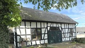 A traditional half-timbered building with a green gate, a stone pathway, and a bench. - Kitchen-living room with bathroom in a historic barn (Hennef)