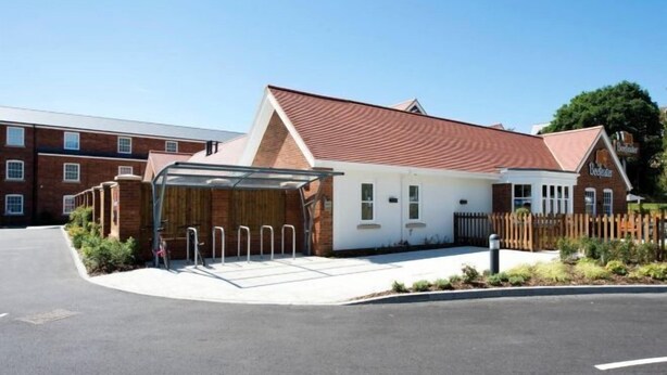 A modern building with a red-tiled roof, a covered entrance, and a brick facade. - Farnham (Farnham)