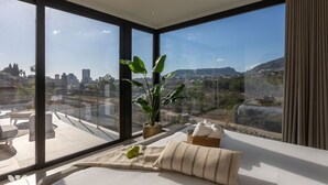 Een moderne kamer met grote ramen, een bed, een plant en uitzicht op een stadsbeeld.