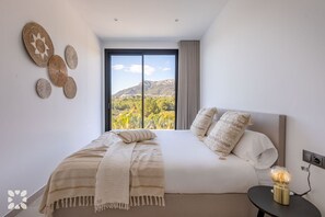 Ein Schlafzimmer mit einem großen Bett, Blick auf eine gebirgige Landschaft und einem Nachttisch mit einer Lampe.