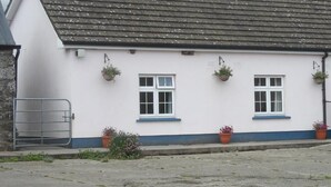 Un bâtiment blanc avec un toit gris, deux fenêtres et des plantes en pot.