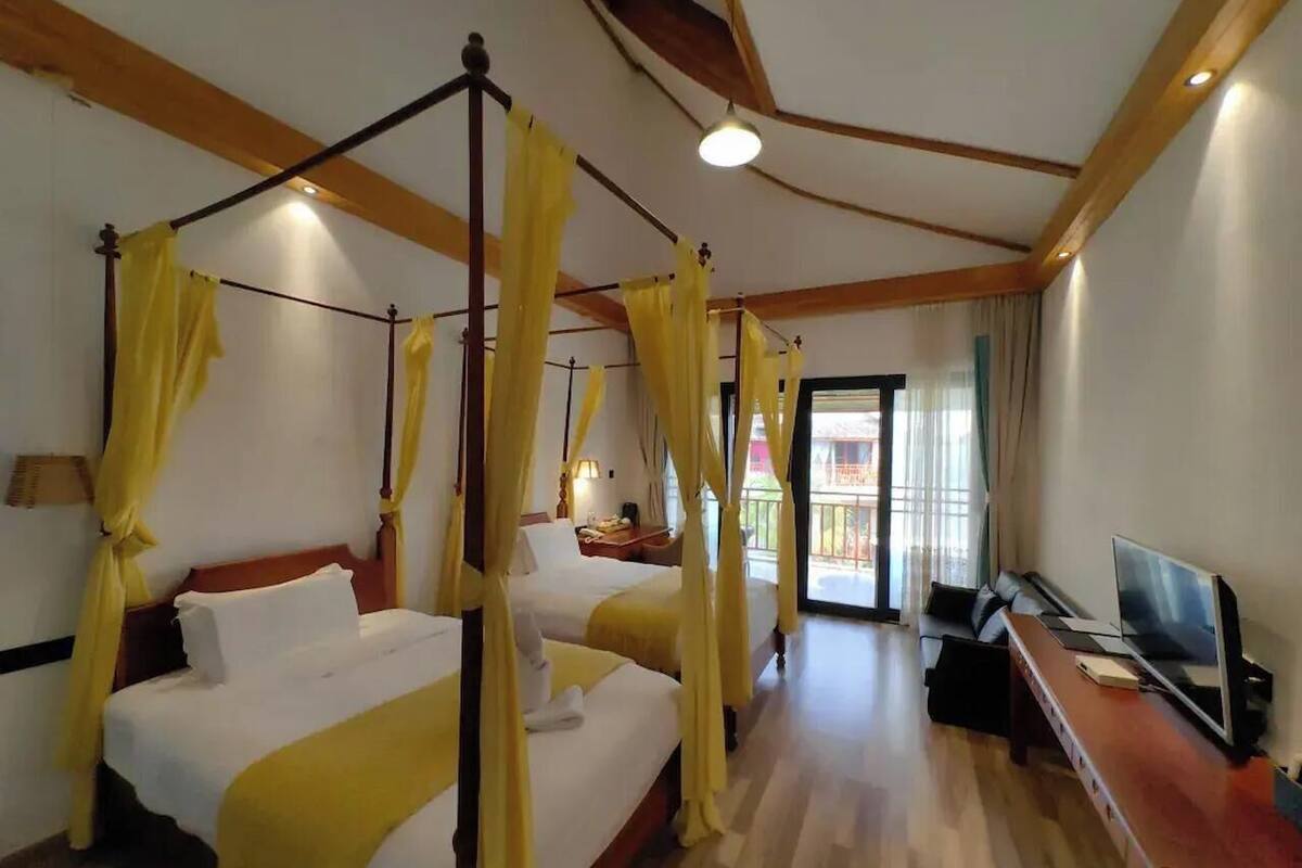 A hotel room with a four-poster bed, a sofa, a TV, and a balcony with curtains.
