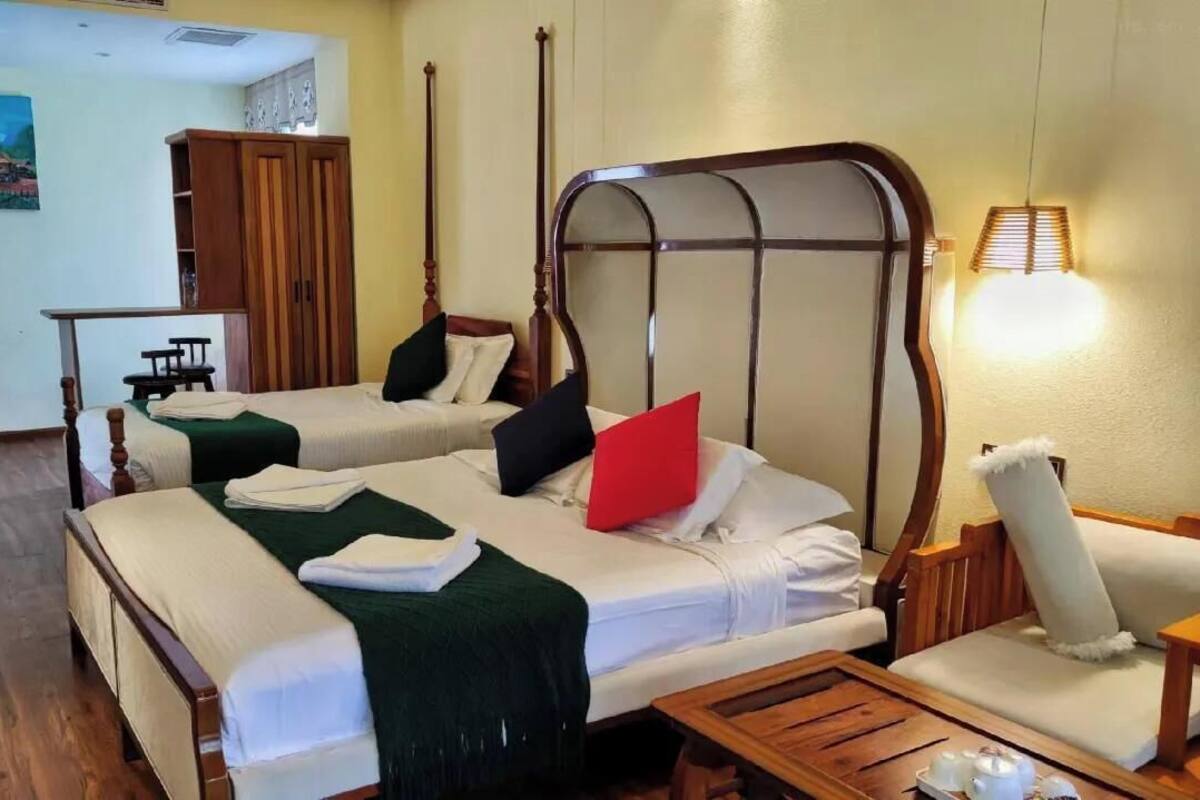 A hotel room with two beds, a wooden wardrobe, a chair, and a small table.