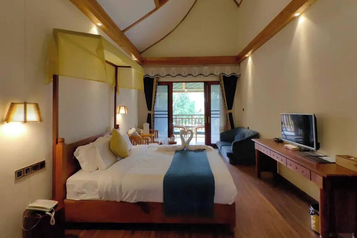 A hotel room with a bed, bedside lamps, a desk with a television, and a view of the outdoors.