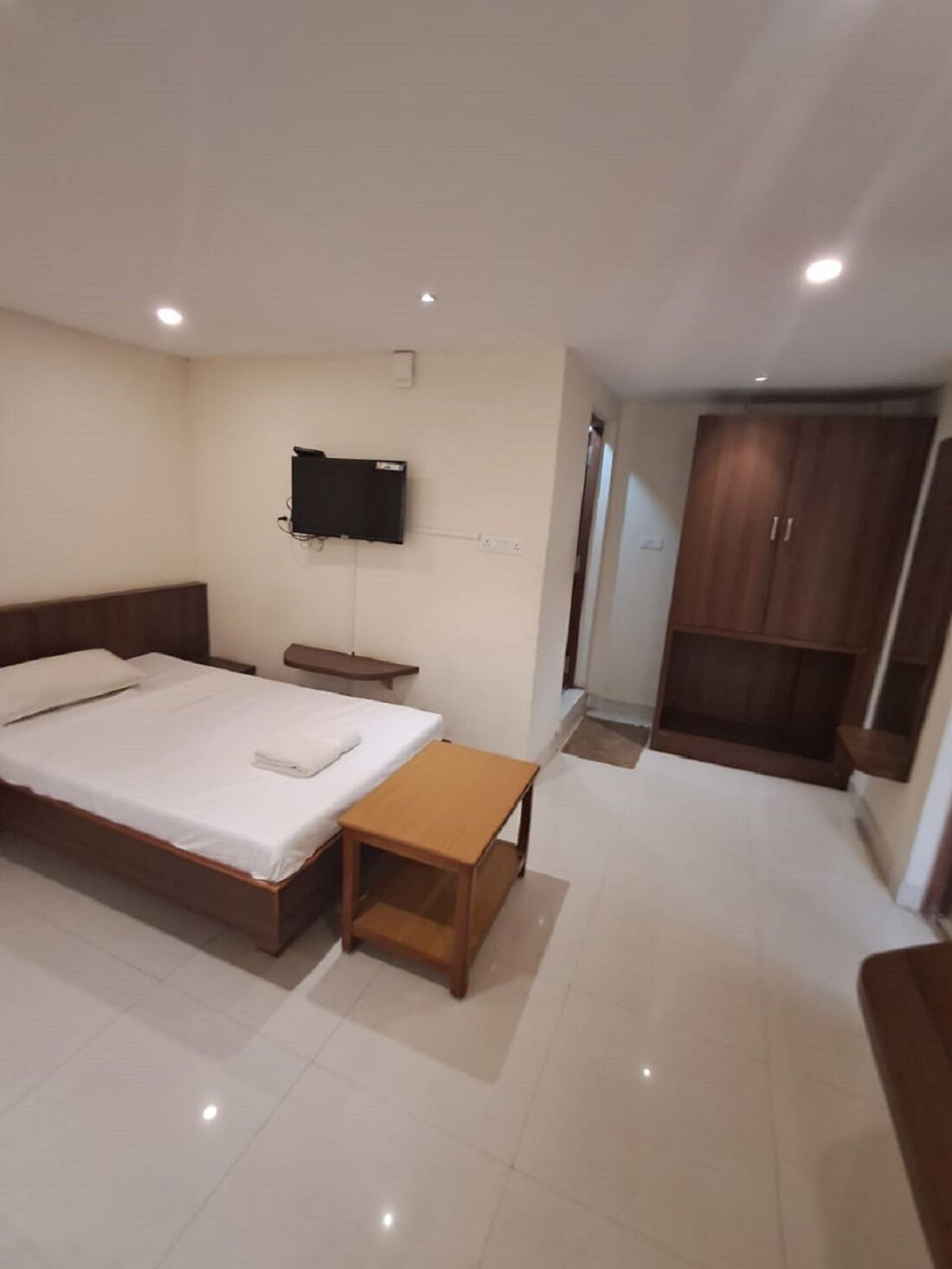 A hotel room with a bed, bedside table, TV, wardrobe, and a small bathroom.