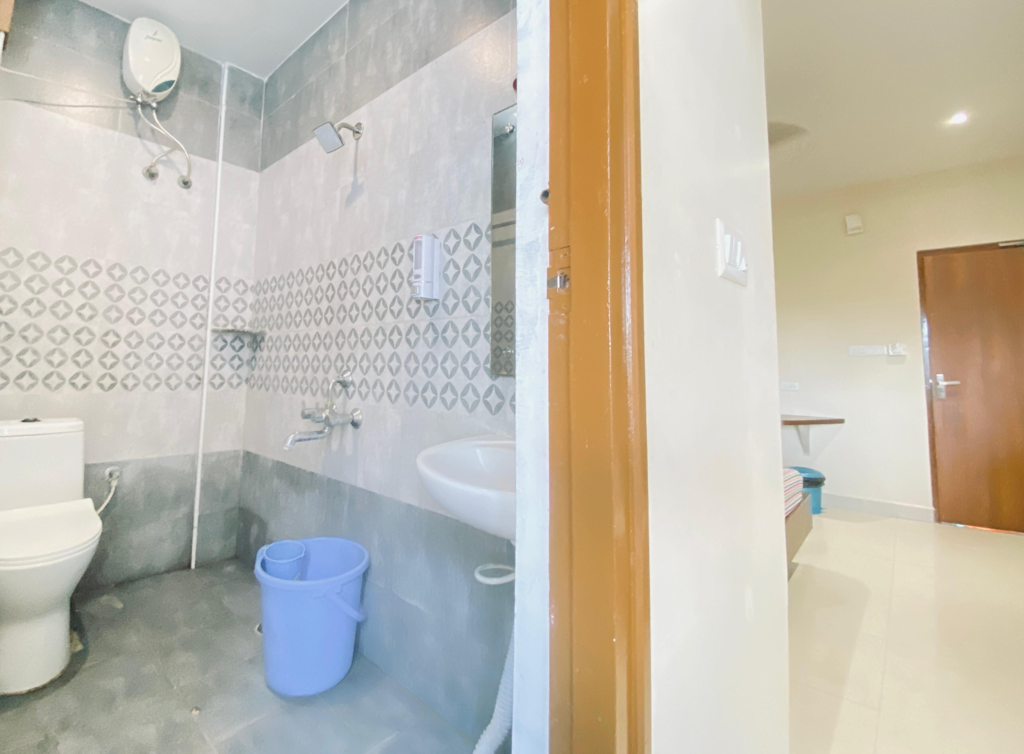 A bathroom with a toilet, bidet, and sink, a blue bucket, and a shower with a handheld showerhead.