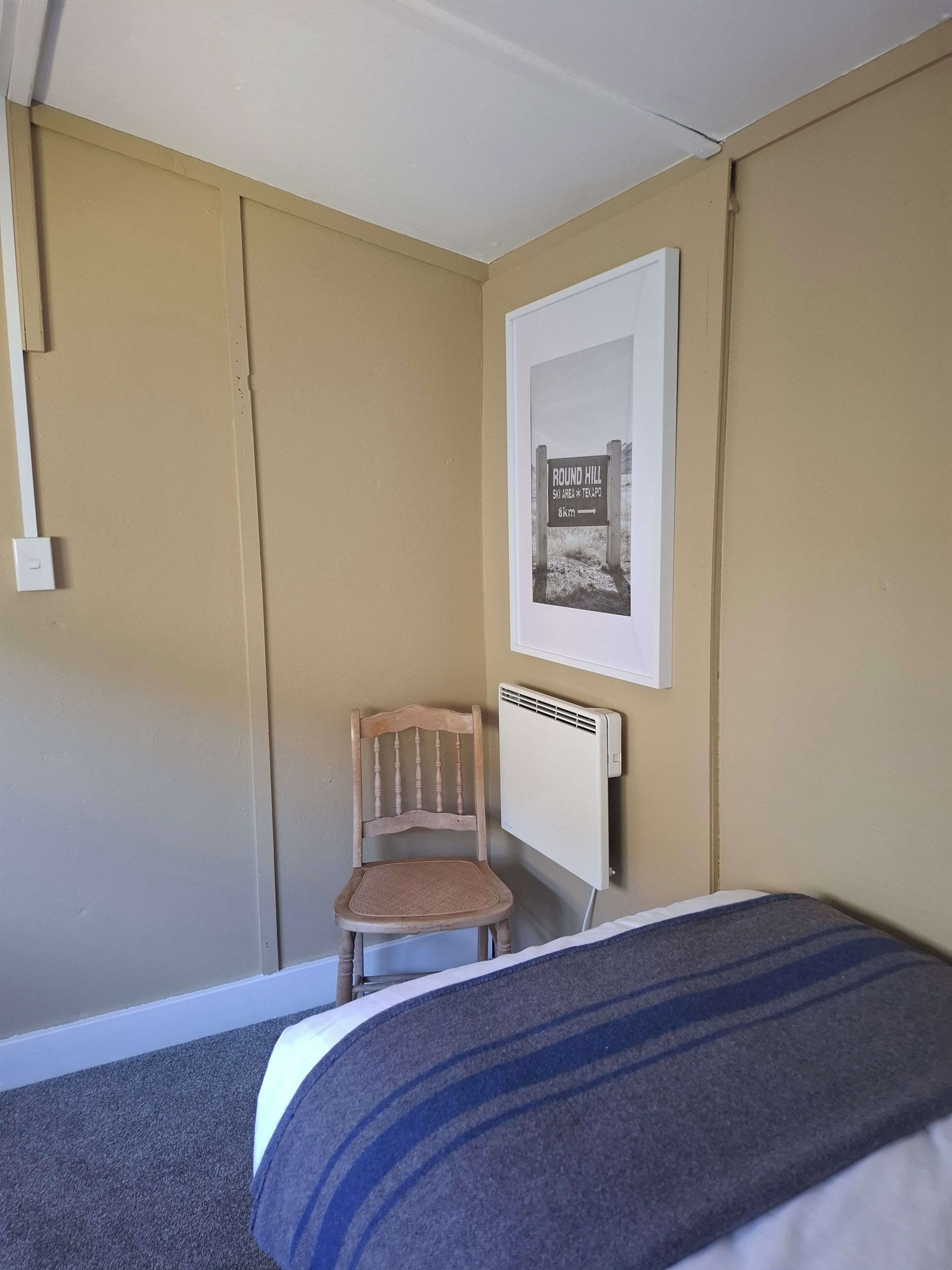 A bedroom with a bed, a chair, a radiator, and a framed picture on the wall.