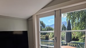 Et værelse med en skydedør, der fører til en terrasse med bord og stole, en trækommode med et fjernsyn ovenpå og en fletkurv.