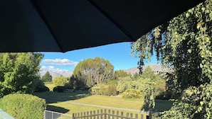 Udsigt fra en overdækket terrasse med et træhegn, en græsplæne og træer i baggrunden.