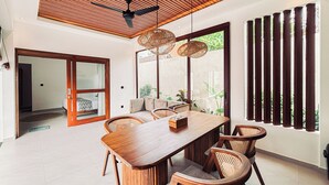 Un comedor moderno con una mesa y sillas de madera, un ventilador de techo y ventanas amplias con persianas verticales.