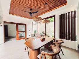 Un comedor moderno con una mesa y sillas de madera, un ventilador de techo y ventanas amplias con persianas verticales.