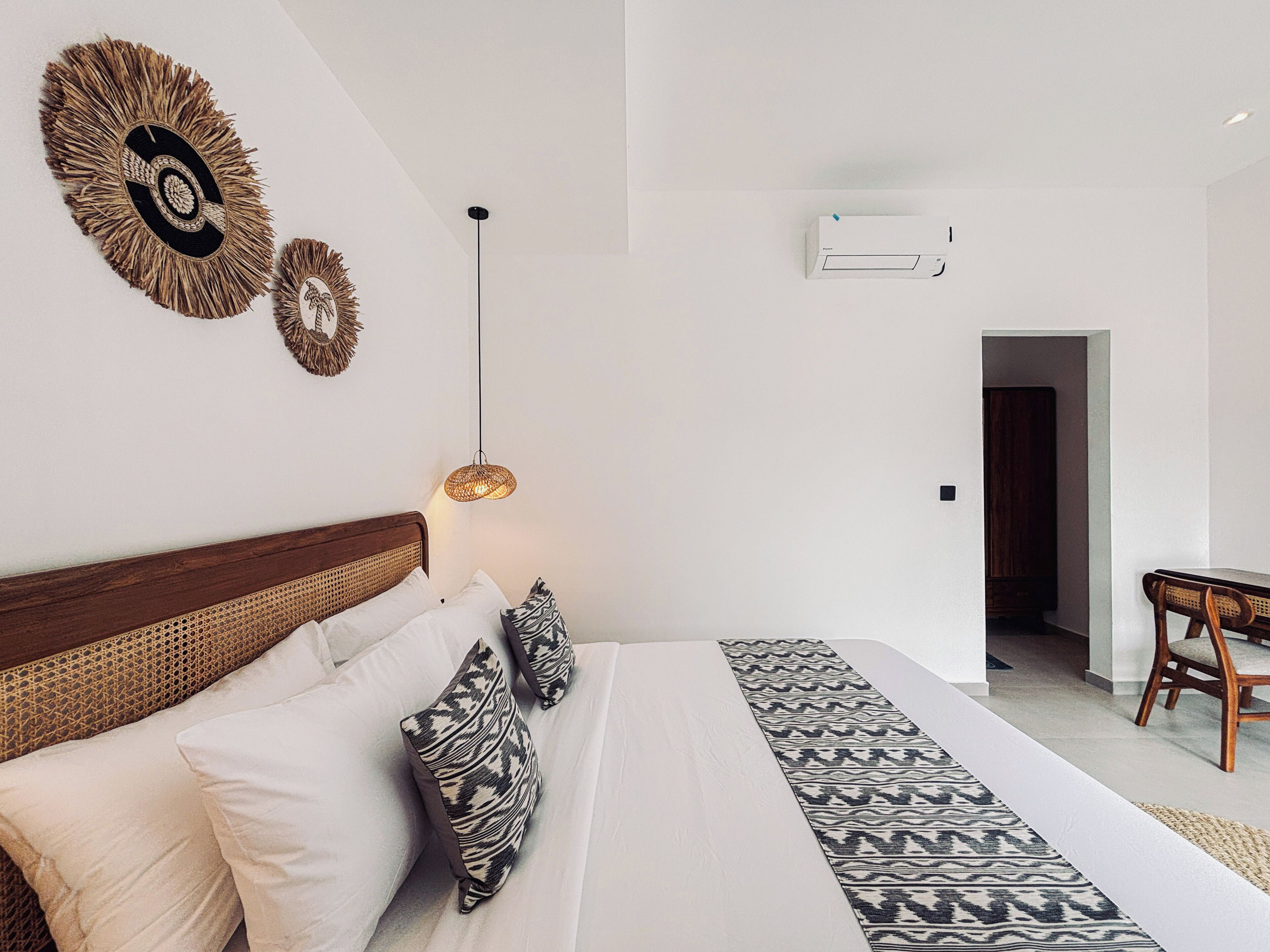 A bedroom with a bed, pillows, a hanging light, and wall art.