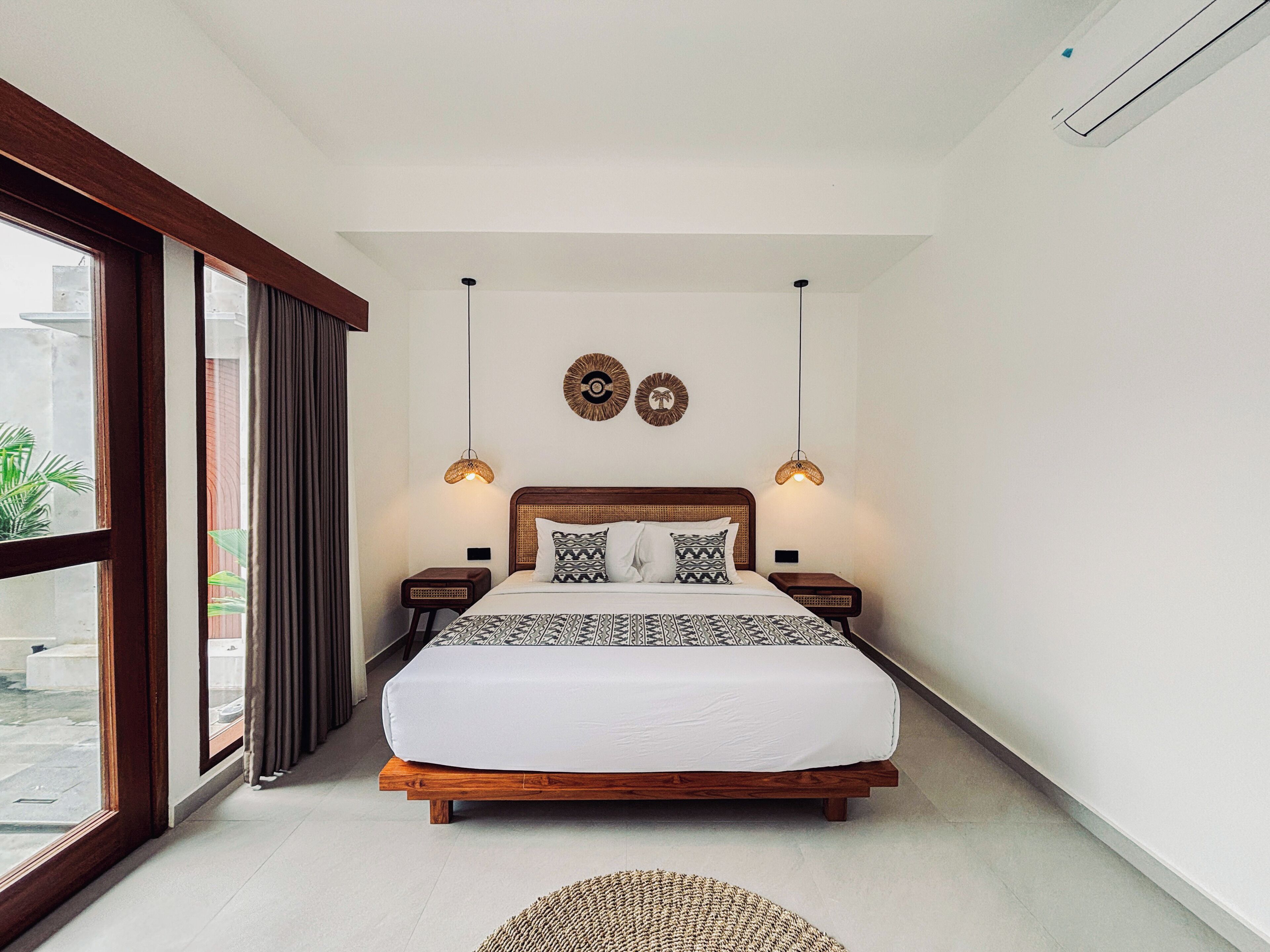 A bedroom with a large bed, two wall-mounted lamps, and a view through a sliding door.