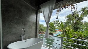 Un baño moderno con una bañera independiente, ducha y vistas a un tobogán acuático y vegetación.