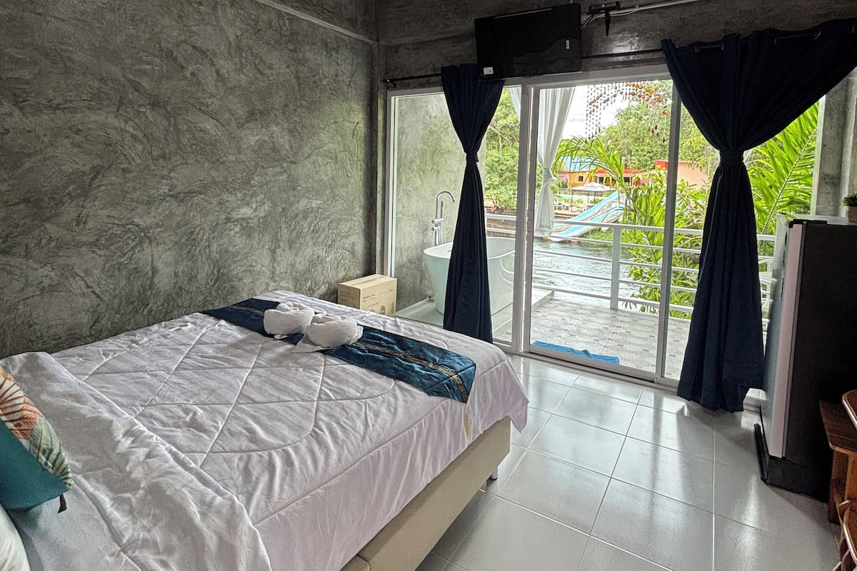 Un dormitorio moderno con una cama grande, una lámpara en el techo y vistas a una piscina y vegetación.