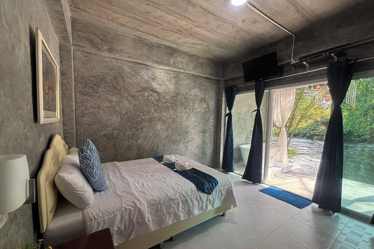 Un dormitorio con cama, mesita de noche, lámpara y vistas a un jardín a través de una puerta corredera.
