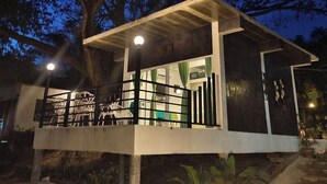 Un edificio pequeño y moderno con balcón, rodeado de árboles y un cielo nocturno.