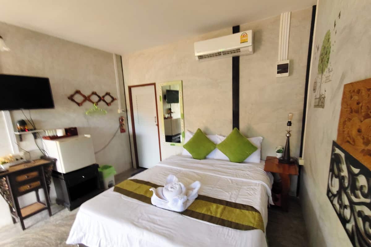Habitación de hotel con cama, unidad de aire acondicionado, escritorio con computadora y televisor en la pared.
