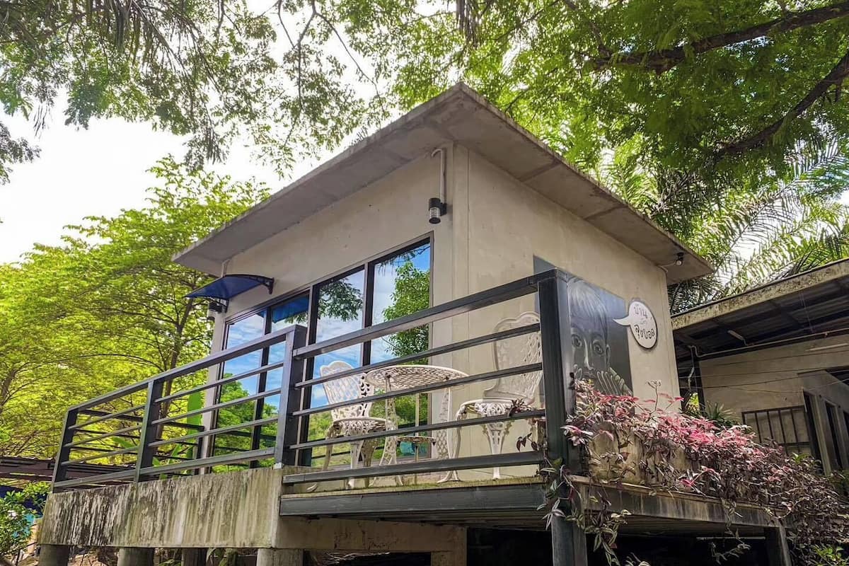 Un edificio pequeño y elevado con balcón, ventanas grandes y barandilla metálica.