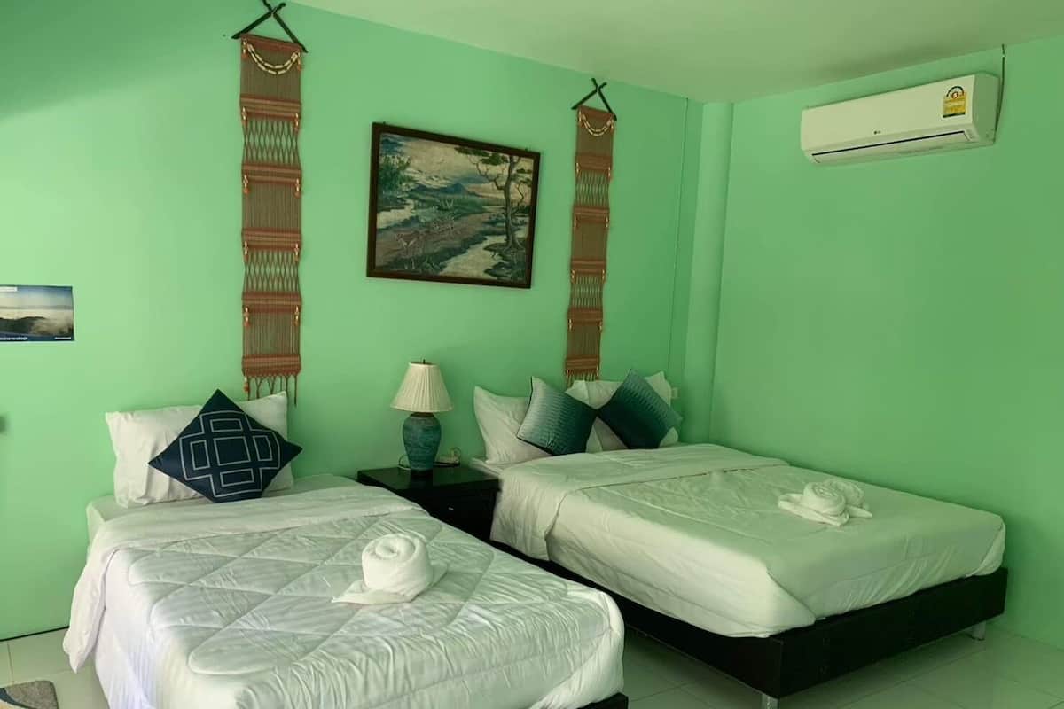 Una habitación con dos camas, un cuadro, un tapiz tejido, una lámpara y aire acondicionado.