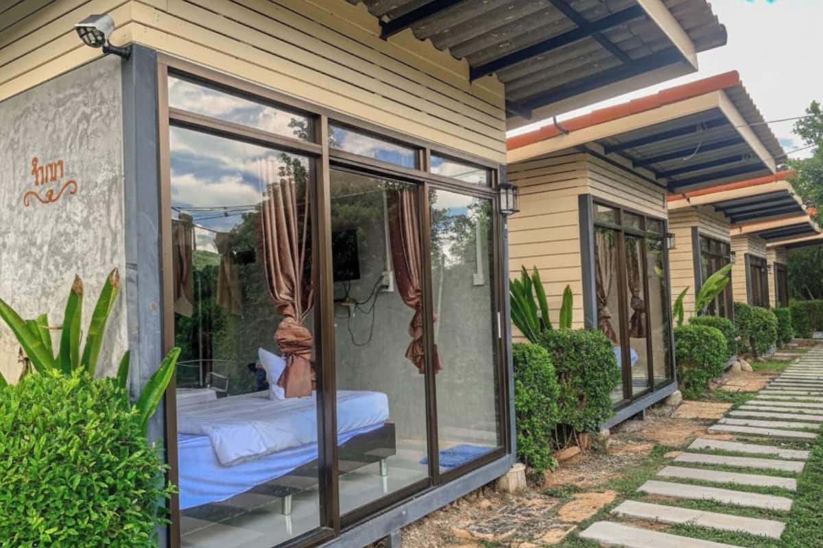 Un dormitorio moderno al aire libre con cerramiento de vidrio, una cama y vistas del jardín circundante.