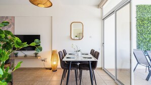 A dining area with a table set for four, a television on the wall, and a large window with a view of greenery. - Yellow Canvas 2-BR & Balcony in Larnaca (Larnaca)