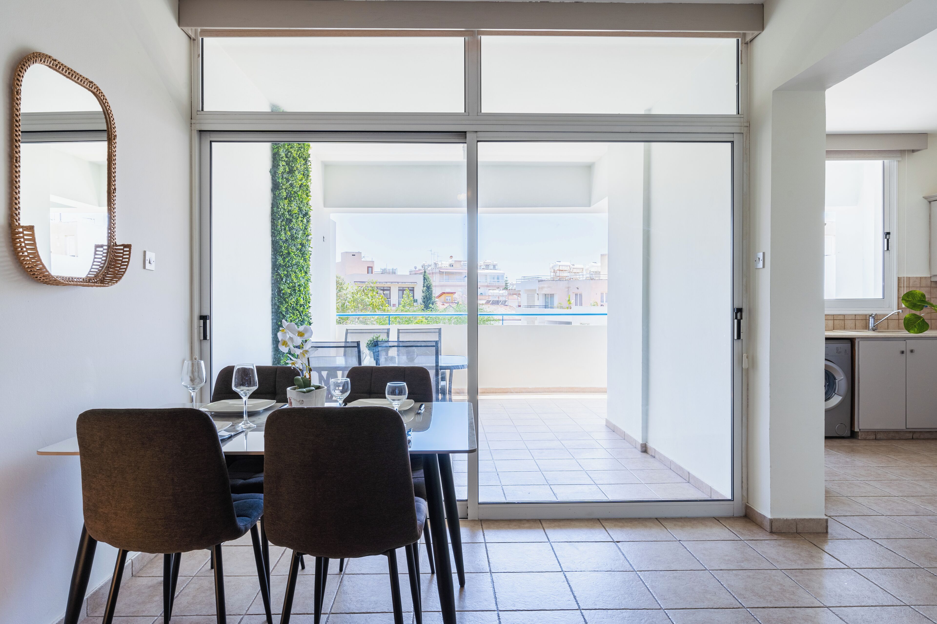 Ein Essbereich mit einem für zwei Personen gedecktem Tisch, einer Schiebetür, die auf einen Balkon führt, und einem durch die Tür sichtbaren Küchenbereich.