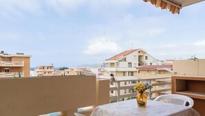 A balcony with a table and chairs, a vase with flowers, and a view of surrounding buildings. - Summer seaview (Alghero)