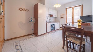 A compact kitchen with white cabinets, a gas stove, and a dining area with a wooden table and chairs. - Summer seaview (Alghero)