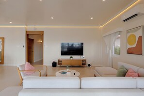 Una sala de estar moderna con un televisor de pantalla plana, sofás blancos, una mesa de centro y un mueble de madera.