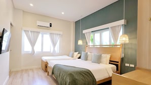 A hotel room with two beds, a desk, a TV, and an air conditioning unit.
