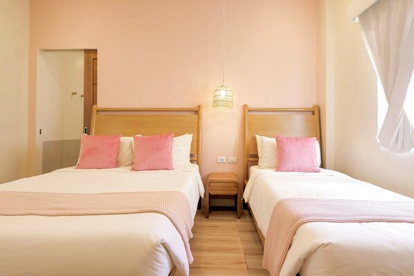 Habitación de hotel con dos camas, suelo de madera, lámpara colgante y una puerta a la izquierda.