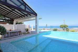 Ein Pool mit Barbereich, überdachtem Sitzbereich und Meerblick.