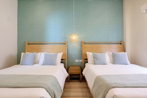 A hotel room with two beds, a small wooden stool, and a wall-mounted light fixture.