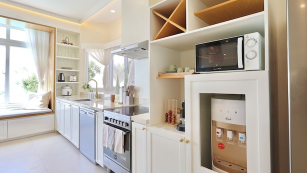A modern kitchen with built-in appliances, a window seat, and a water dispenser.