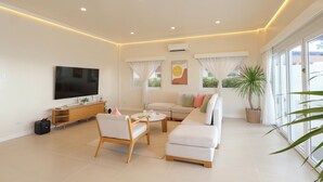 A modern living room with a TV, sofa, armchair, and a potted plant. - Alesea Baroro: Private Beachfront Villa - Pool, Jacuzzi (Bacnotan)