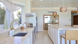 A modern kitchen with a central island, white cabinetry, and a large window with curtains.