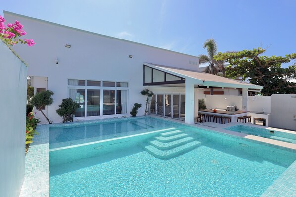 Una casa moderna con piscina, un patio cubierto y una zona de bar.