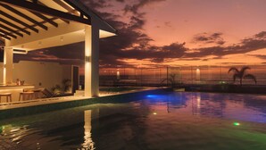 A modern pool area with a sunset view, a covered seating area, and a clear pool.