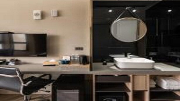 Een moderne hotelkamer met een flatscreen televisie, een ronde spiegel, een wit wastafel en een bureau met een stoel.