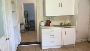 Eine kleine Küche mit weißen Schränken, einem Spülbecken und einem Toaster. Eine Tür führt in einen anderen Raum.