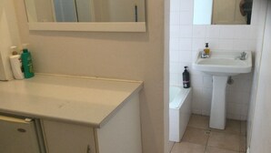 Ein Badezimmer mit weißem Waschbecken, Spiegel und Schrank. Auf der Ablage liegen Pflegeprodukte.