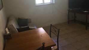 Ein Wohnzimmer mit Holztisch, einer Couch, einem Fernseher auf einem Schrank und einem Fenster.