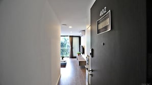 Un pasillo moderno de hotel con una pared oscura, un cartel que indica la habitación 402 y vistas a un balcón con una planta.