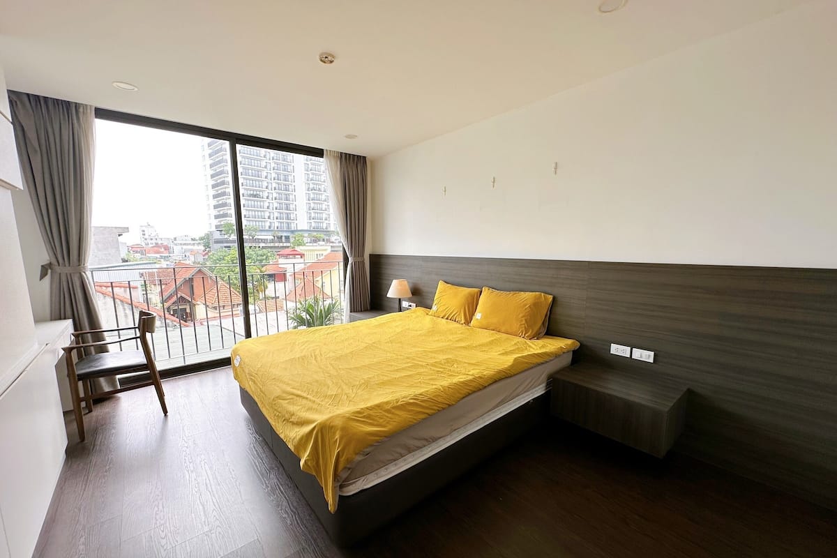 Une chambre d’hôtel avec un grand lit, un bureau et une vue sur les immeubles depuis un balcon.